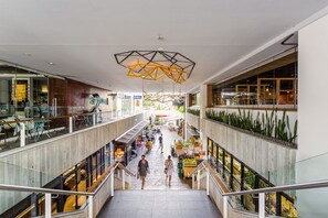 A multi-level shopping mall with a central walkway, glass railings, and a modern ceiling design. - Adina Apartment Hotel Bondi Beach Sydney (Bondi Beach)
