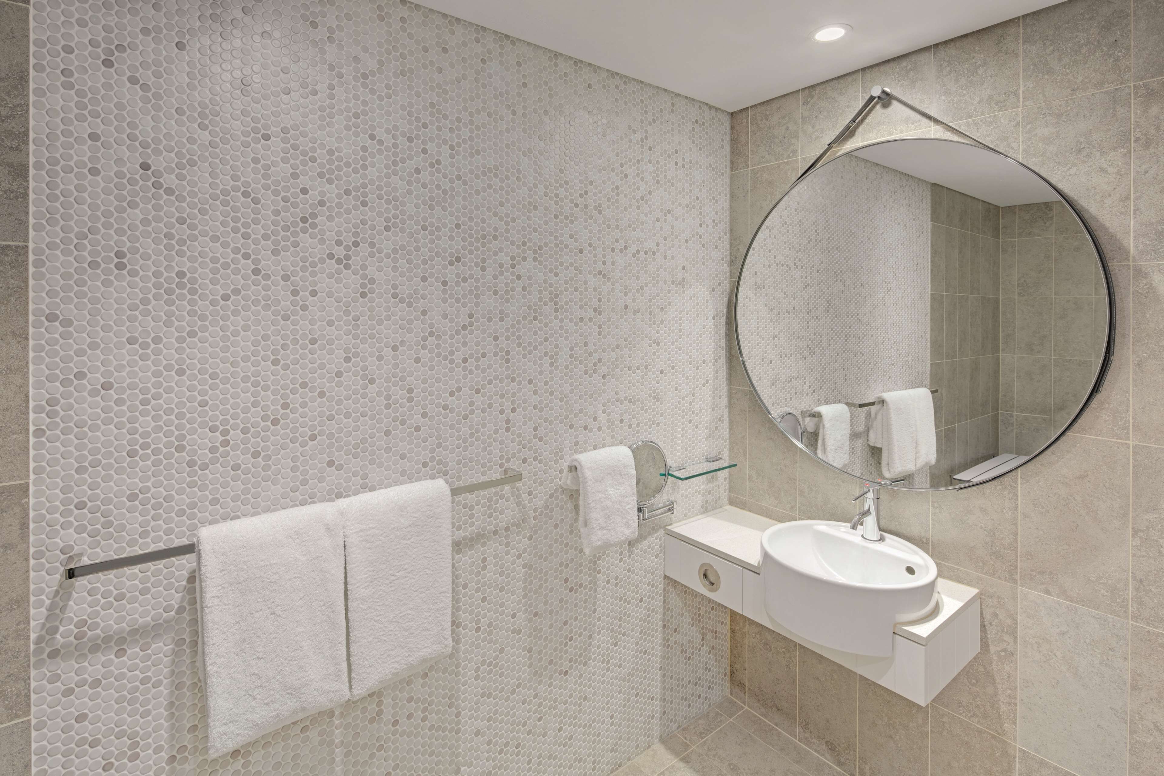 Un bagno moderno con box doccia in vetro, uno specchio rotondo e un lavandino bianco.