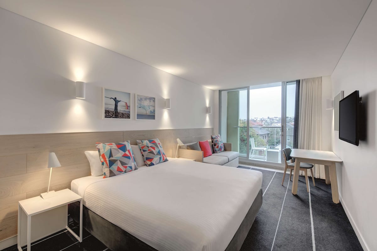 Une chambre d’hôtel moderne, dotée d’un grand lit, d’un bureau et offrant une vue sur la ville.