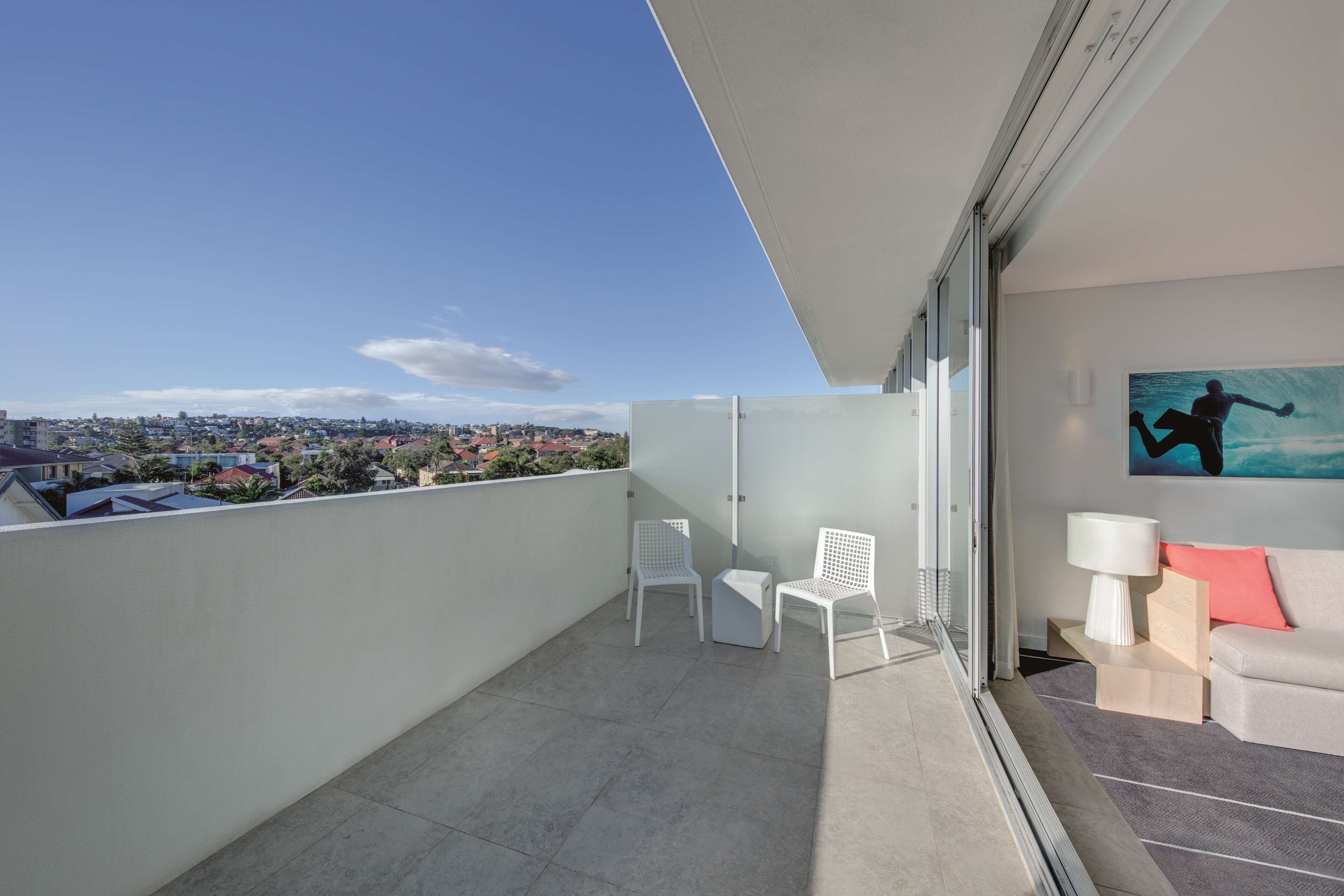 A balcony with a city view, white chairs, a sofa, and a painting.