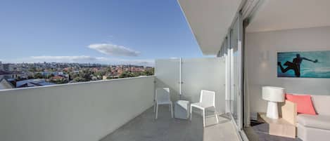 A balcony with a city view, white chairs, a sofa, and a painting.