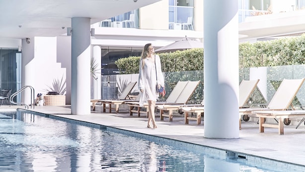 Zona de piscina con sillones de descanso y una persona caminando.