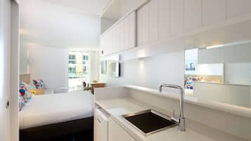 A compact hotel room with a bed, a small kitchenette, a sink, and a mirror.