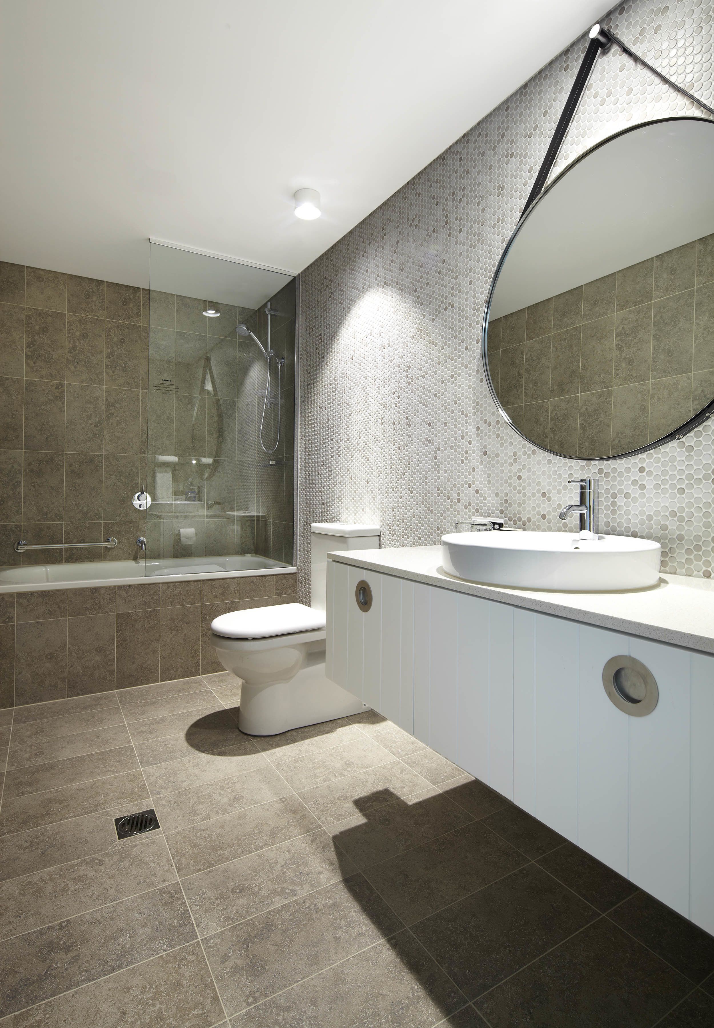 A modern bathroom with a glass-enclosed shower, a white toilet, and a large round mirror above a white sink.