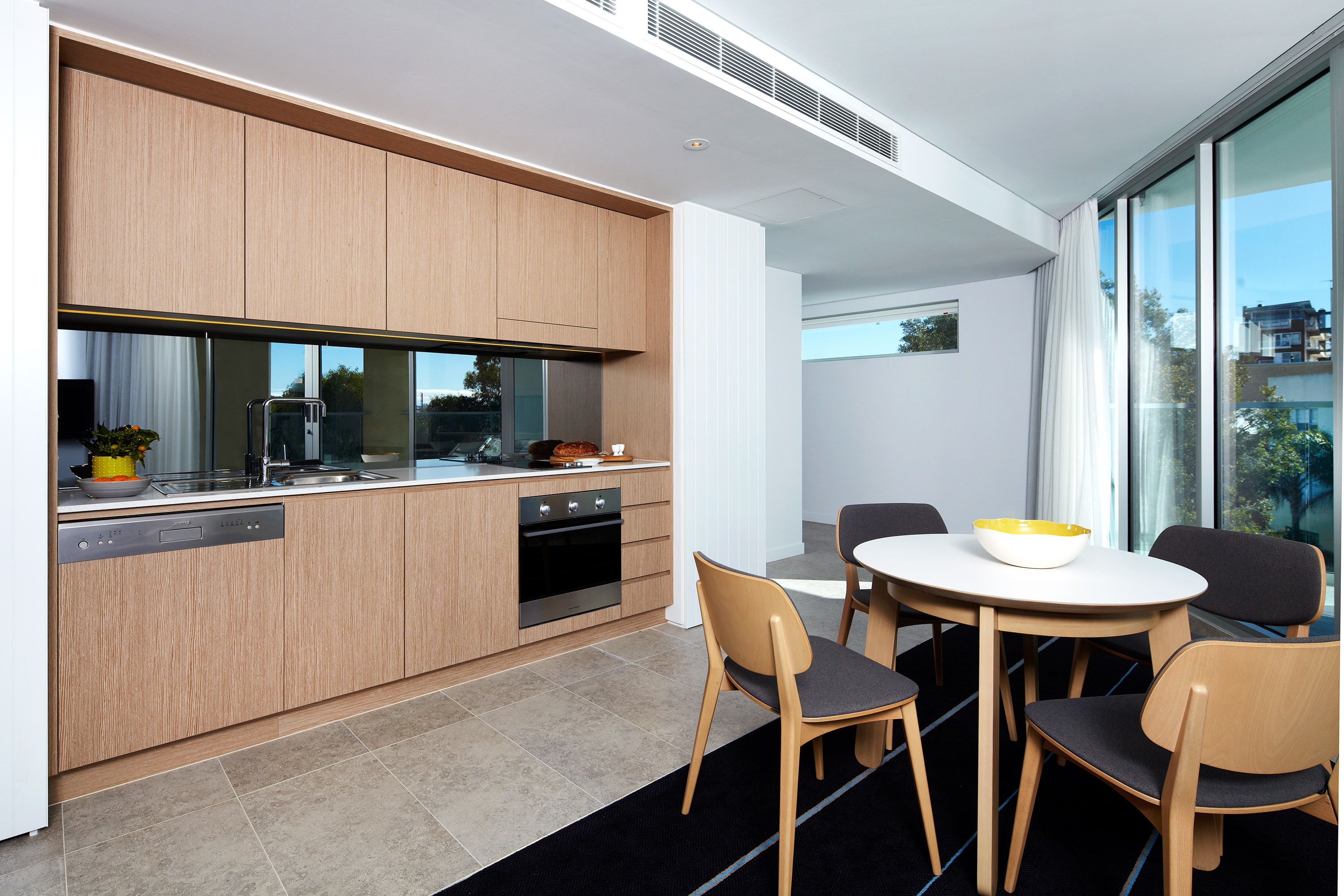 A modern kitchen with wooden cabinets, a dishwasher, and a dining area with a round table and four chairs.