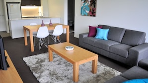 Una sala moderna con un sofá gris, una mesa de centro de madera y un comedor con una mesa y sillas blancas.