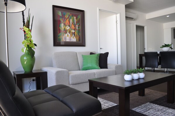A modern living room with a sofa, a coffee table, and a green vase with flowers.
