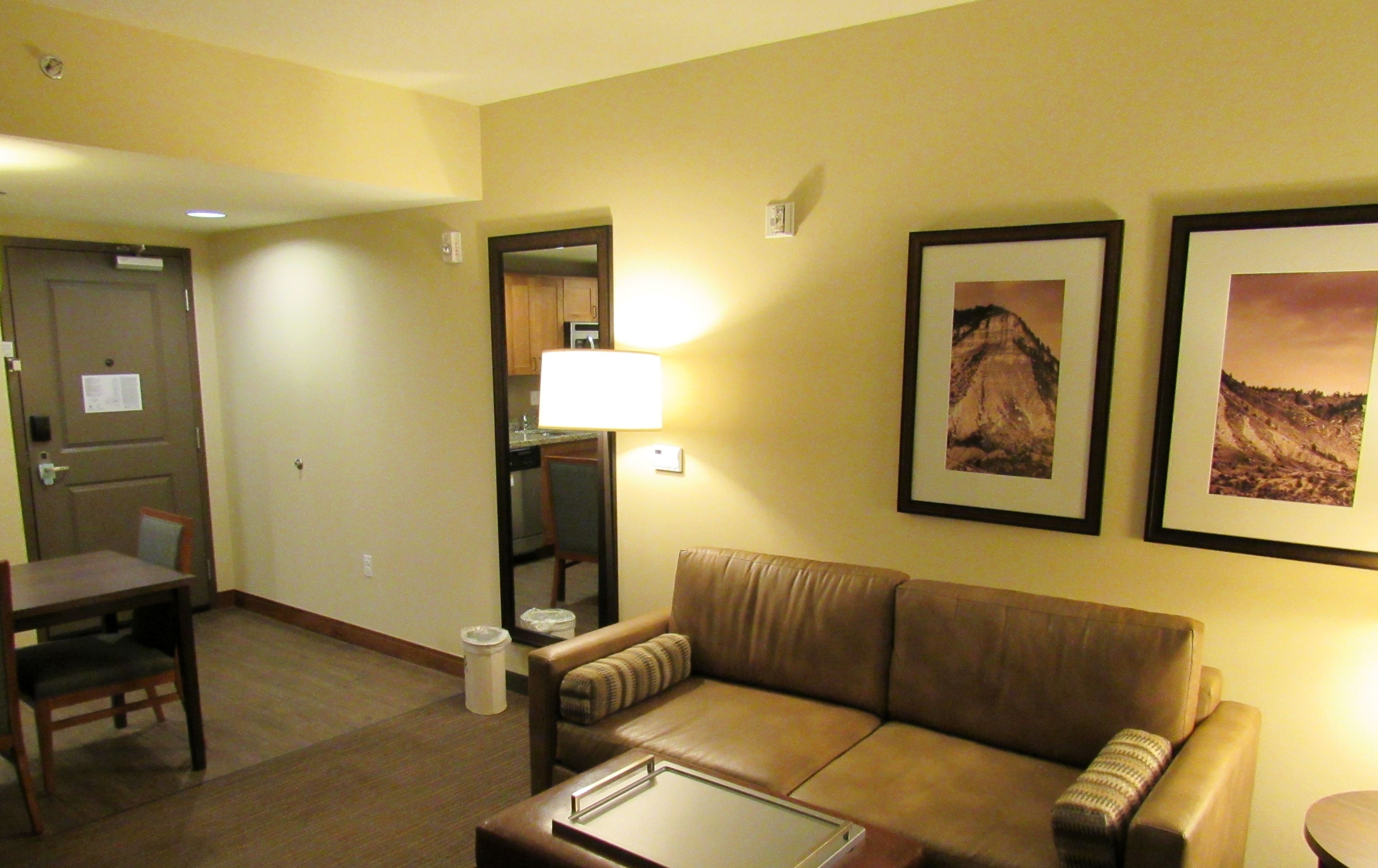 A hotel room with a brown leather sofa, a dining table with chairs, a small coffee table, and two framed pictures on the wall.