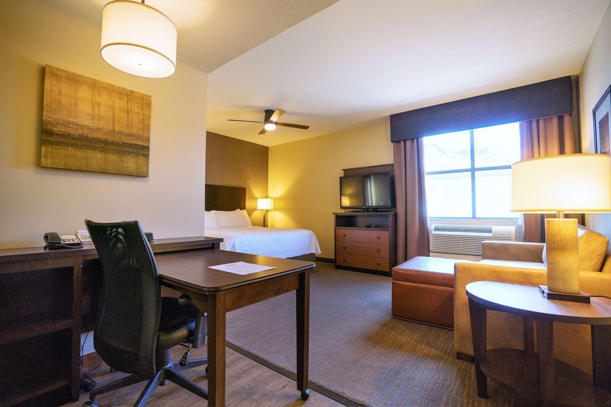 A hotel room with a bed, desk, chair, TV, and a window with curtains.