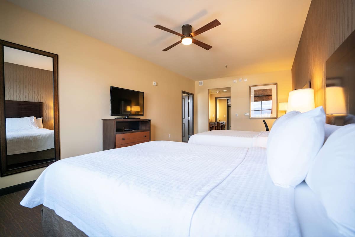 A hotel room with a large bed, a television, a ceiling fan, and a mirror.