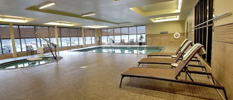 An indoor swimming pool with a view of the parking lot, a sun lounger area, and a sign indicating a 'Living' area.