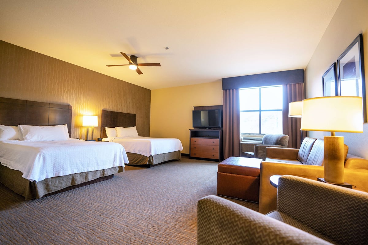 A hotel room with two beds, a TV, a sofa, and a desk.