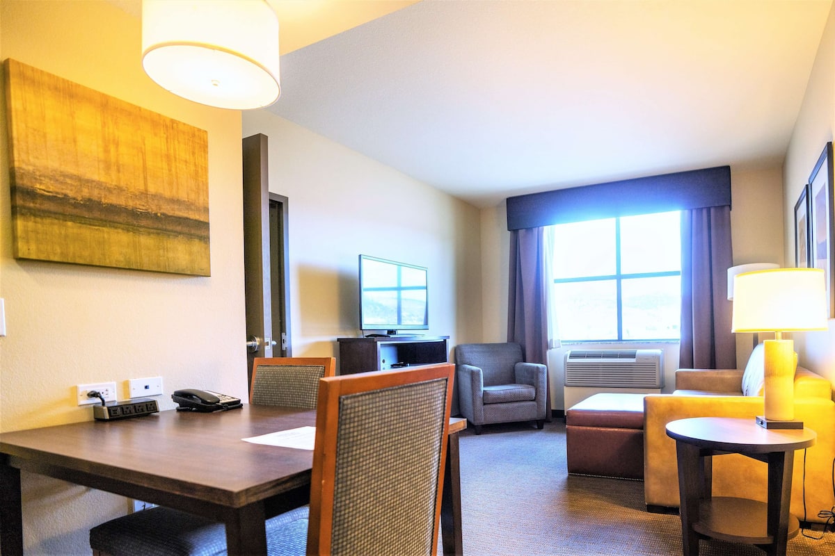 A hotel room with a wooden desk, a television, a sofa, and a lamp.