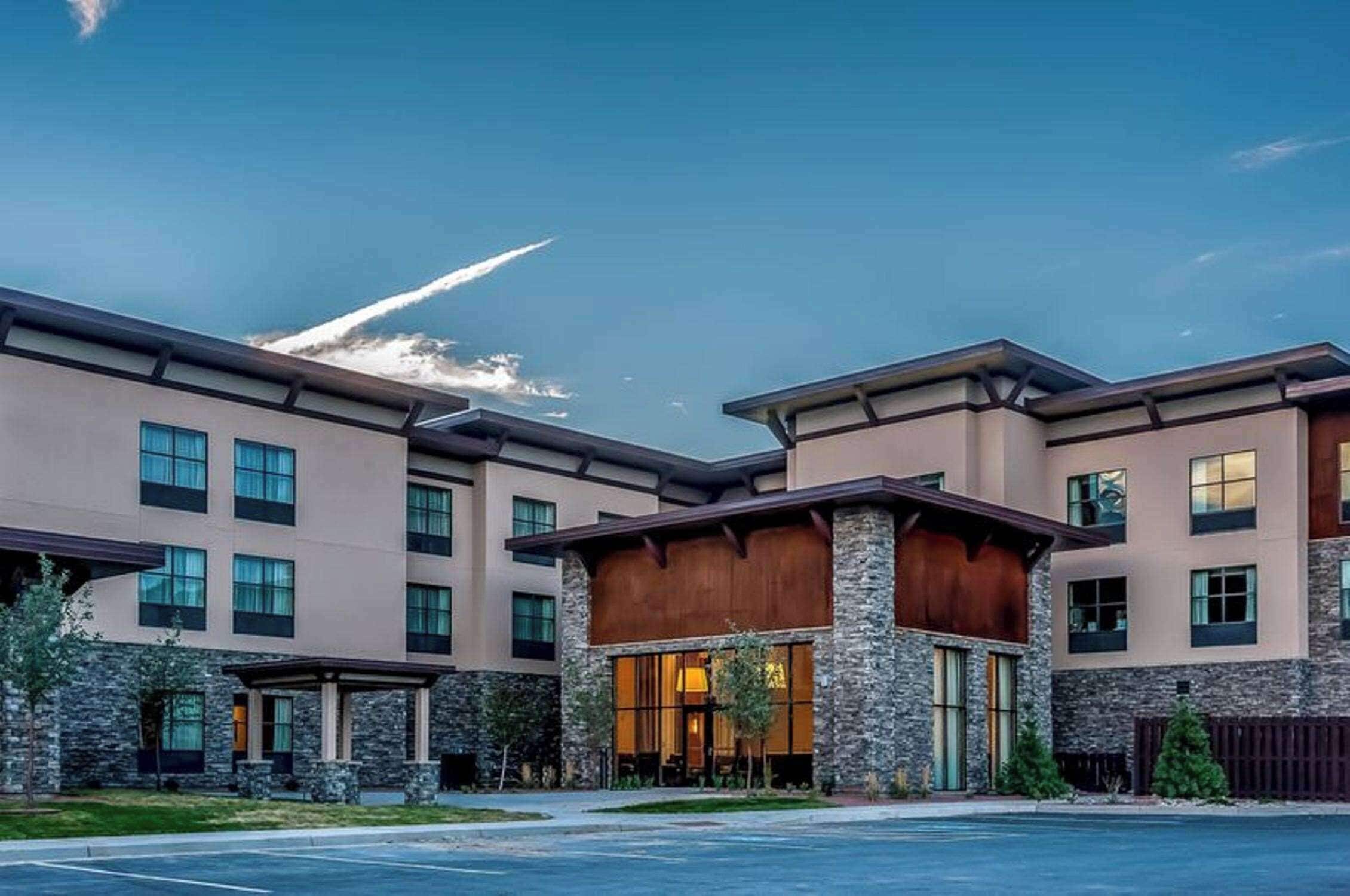A multi-story hotel with a modern design, featuring a mix of stone and wood facade, large windows, and a covered entrance area.