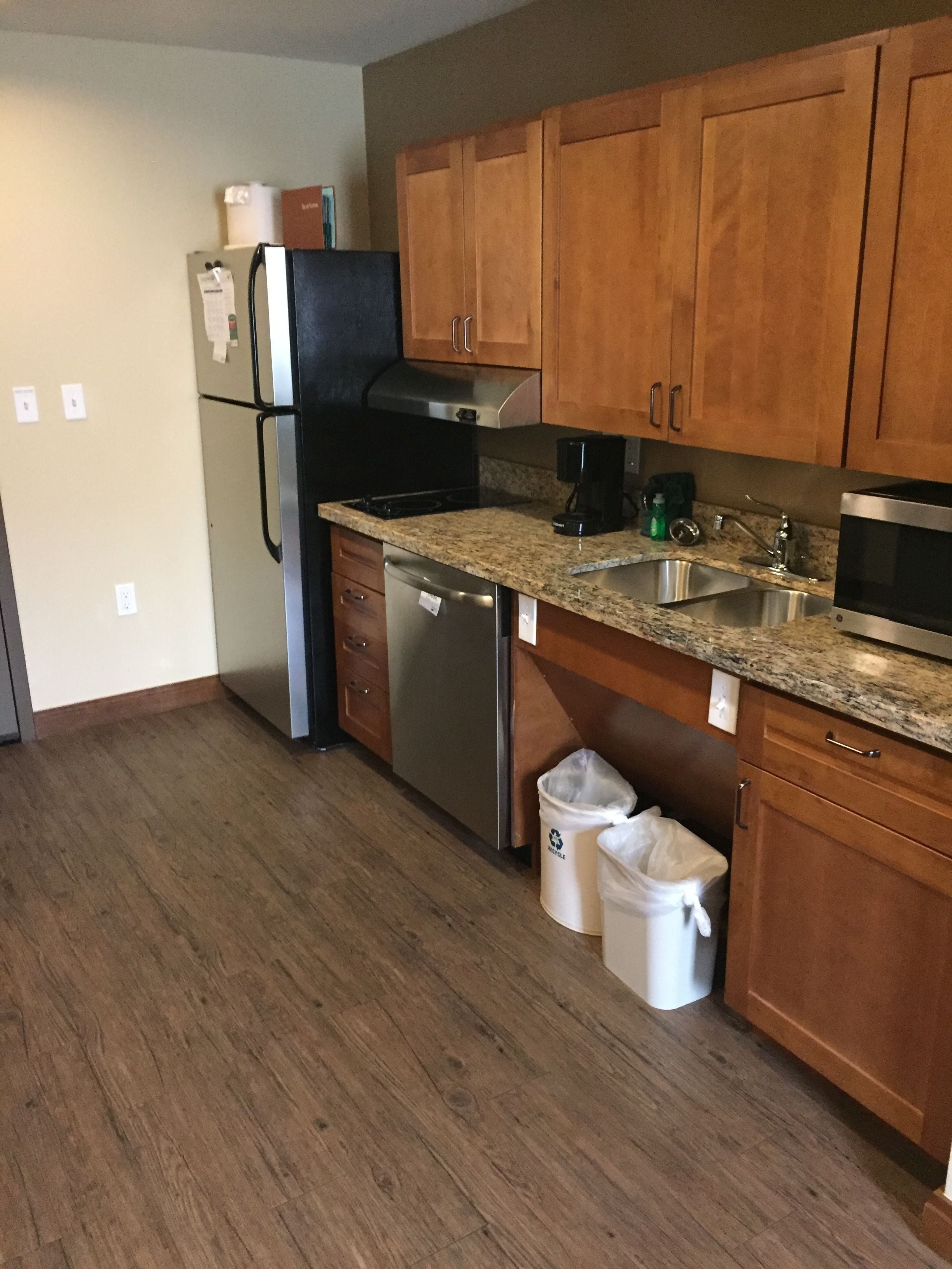 A kitchen with wooden cabinets, a stainless steel refrigerator, a dishwasher, a sink, and a microwave.