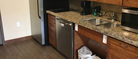 A kitchen with wooden cabinets, a stainless steel refrigerator, a dishwasher, a sink, and a microwave.