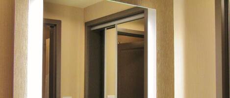 A hotel bathroom with a granite countertop sink, a large mirror, and a visible door leading to another room.