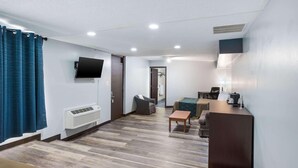 Une chambre d’hôtel équipée d’un téléviseur à écran plat fixé au mur, d’un bureau avec une chaise, d’une petite table et d’un lit recouvert d’une courtepointe verte.