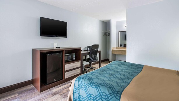 Une chambre d’hôtel comprenant un lit, un bureau avec une chaise, une télévision, un four à micro-ondes et un petit réfrigérateur.