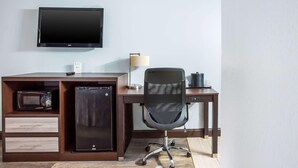 Un espace de bureau moderne équipé d’un téléviseur à écran plat, d’un four à micro-ondes, d’un mini-réfrigérateur, d’un bureau, d’une chaise et d’une lampe.