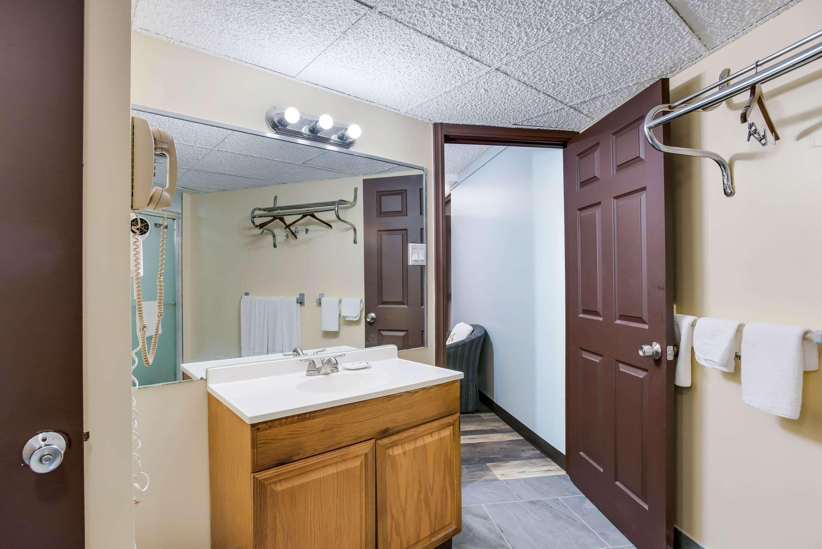 Un baño con lavamanos, espejo, toallero y una puerta que da a otra habitación.