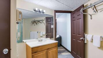 Un baño con lavamanos, espejo, toallero y una puerta que da a otra habitación.