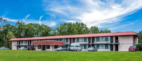 A motel with a red roof, multiple balconies, and a parking lot with several cars.