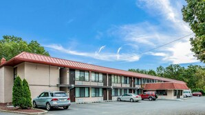Un motel avec un toit rouge, plusieurs places de stationnement et un petit arbre devant.