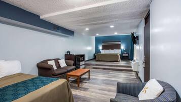 Habitación de hotel con cama, sofá, una mesita, televisión y baño a la vista.