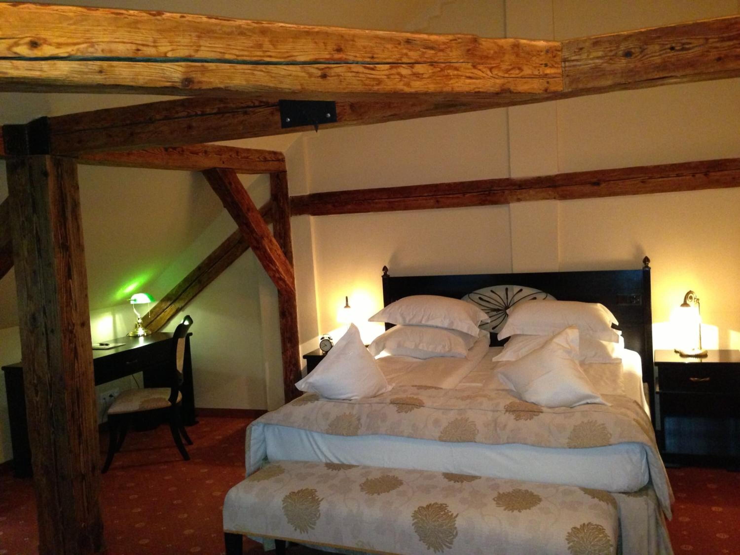 Un dormitorio con cama, vigas de madera, un escritorio y una silla.