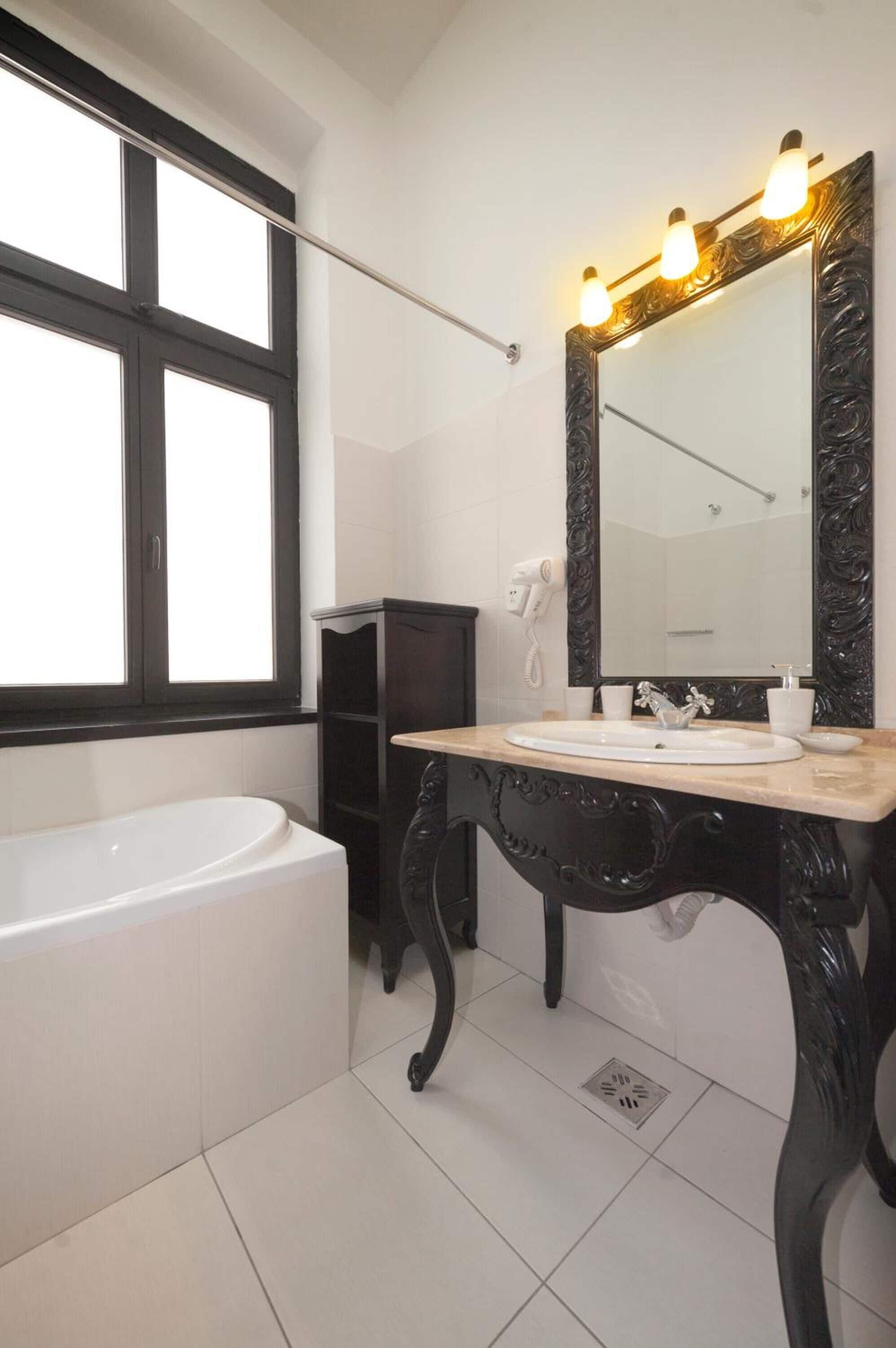 A bathroom with a bathtub, a vanity with a mirror, and a window.