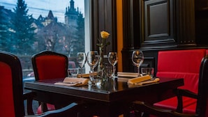 Una mesa de comedor dispuesta con copas de vino, un florero con una rosa amarilla y un mantel doblado.