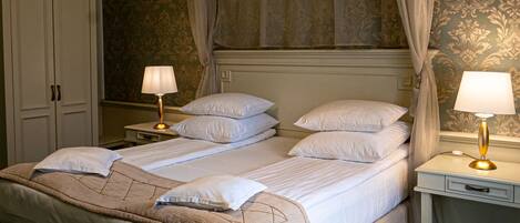 Una cama con dosel con ropa blanca, una alfombra estampada en verde y un candelabro.
