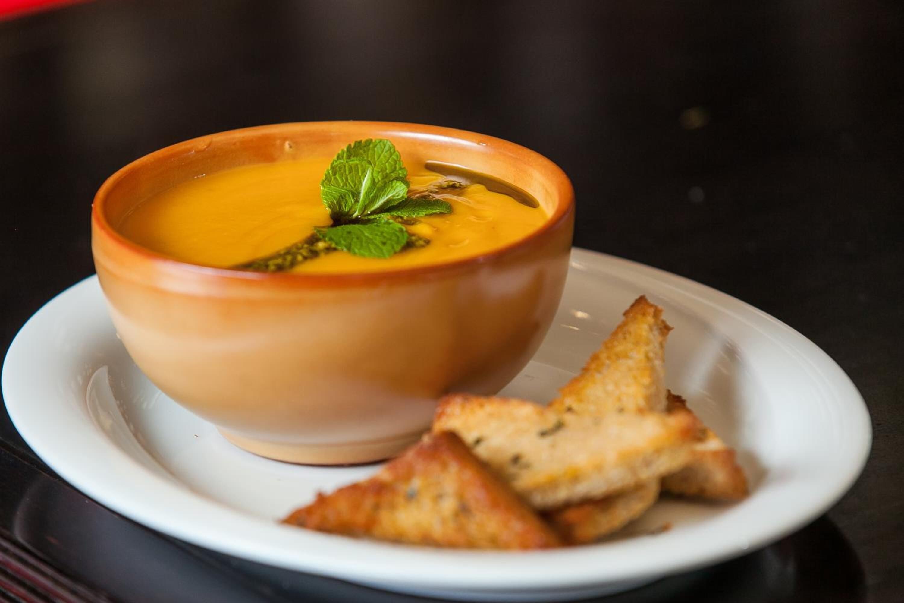 Un tazón de sopa con un adorno sobre un plato blanco, acompañado de trozos de pan tostado.