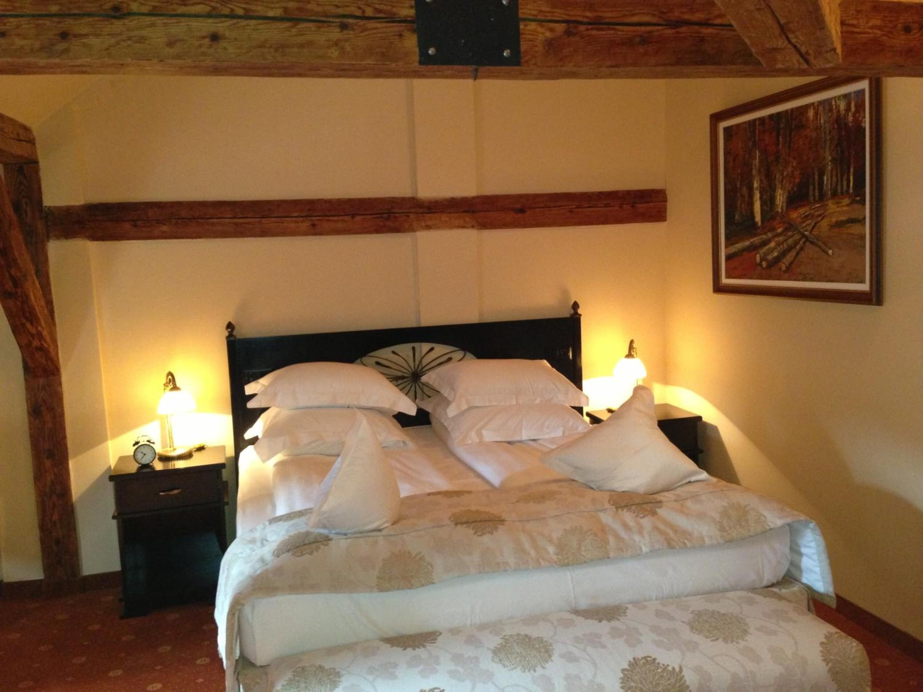 A neatly made bed with white linens and a floral-patterned duvet, two bedside tables with lamps, and a painting on the wall.