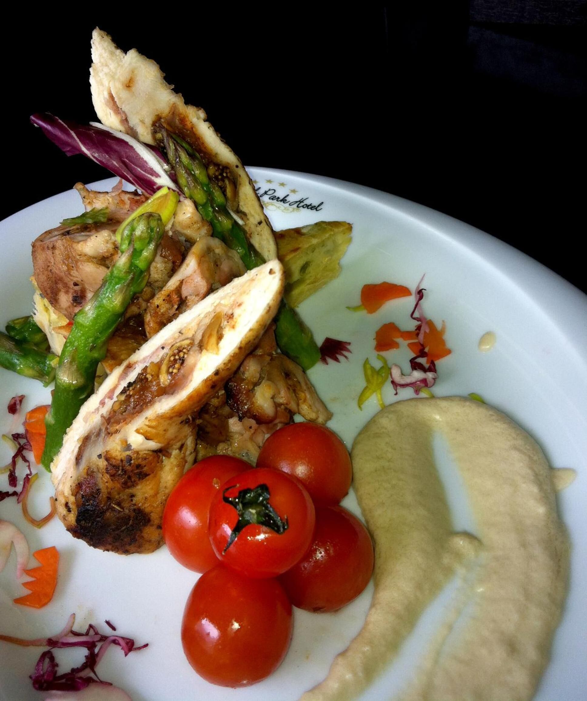Un plato con pollo a la parrilla, espárragos, tomates cherry y hummus.