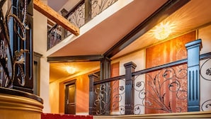 Una imponente escalera con peldaños cubiertos de alfombra roja y barandales de metal ornamentados.