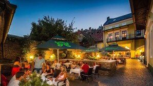 Un espacio de comedor al aire libre con mesas, sillas, sombrillas y un camino de ladrillo.