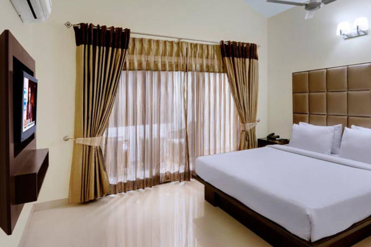 A hotel room with a large bed, a flat-screen TV mounted on the wall, and a ceiling fan.