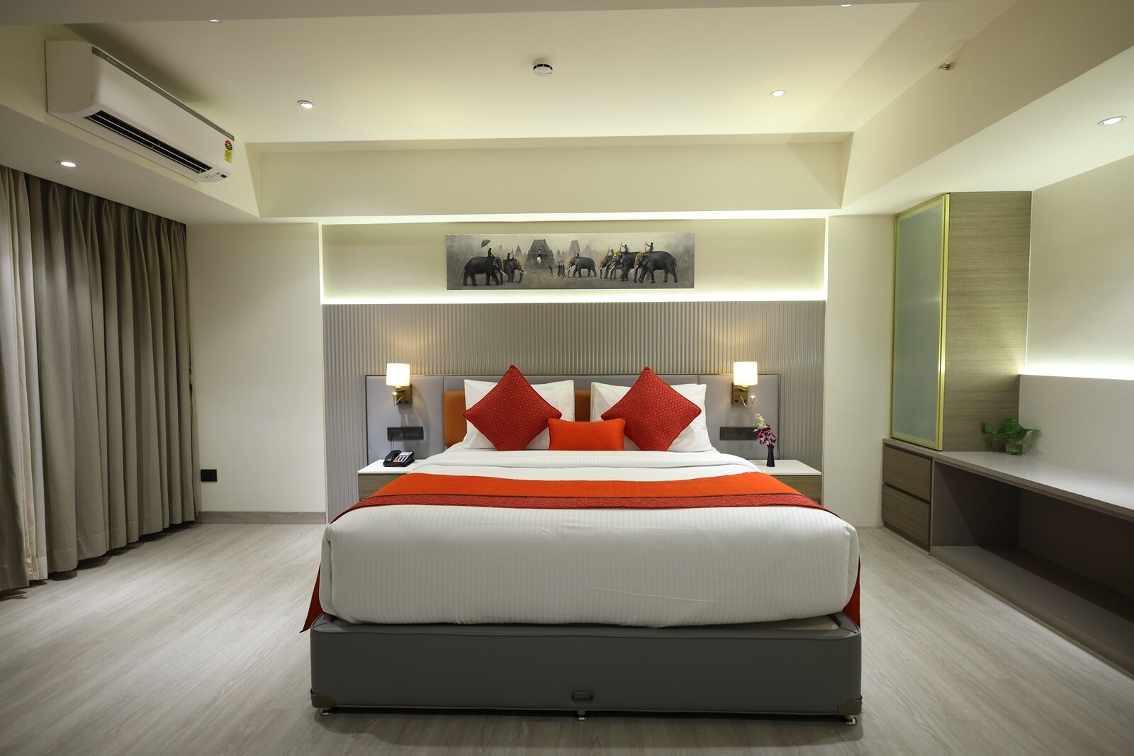 A modern hotel room with a large bed, a painting above the bed, and a desk with a lamp.