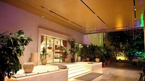 A modern lobby with a reception desk, potted plants, and a view of a tree through a glass wall. - Marigold- Newly Renovated Hotel (Rahata)