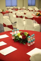 Una sala conferenze con tavoli rotondi, sedie bianche e tovaglie rosse.