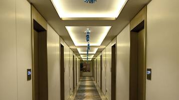A long, well-lit hallway with a patterned carpet, doors on both sides, and a hanging light fixture.