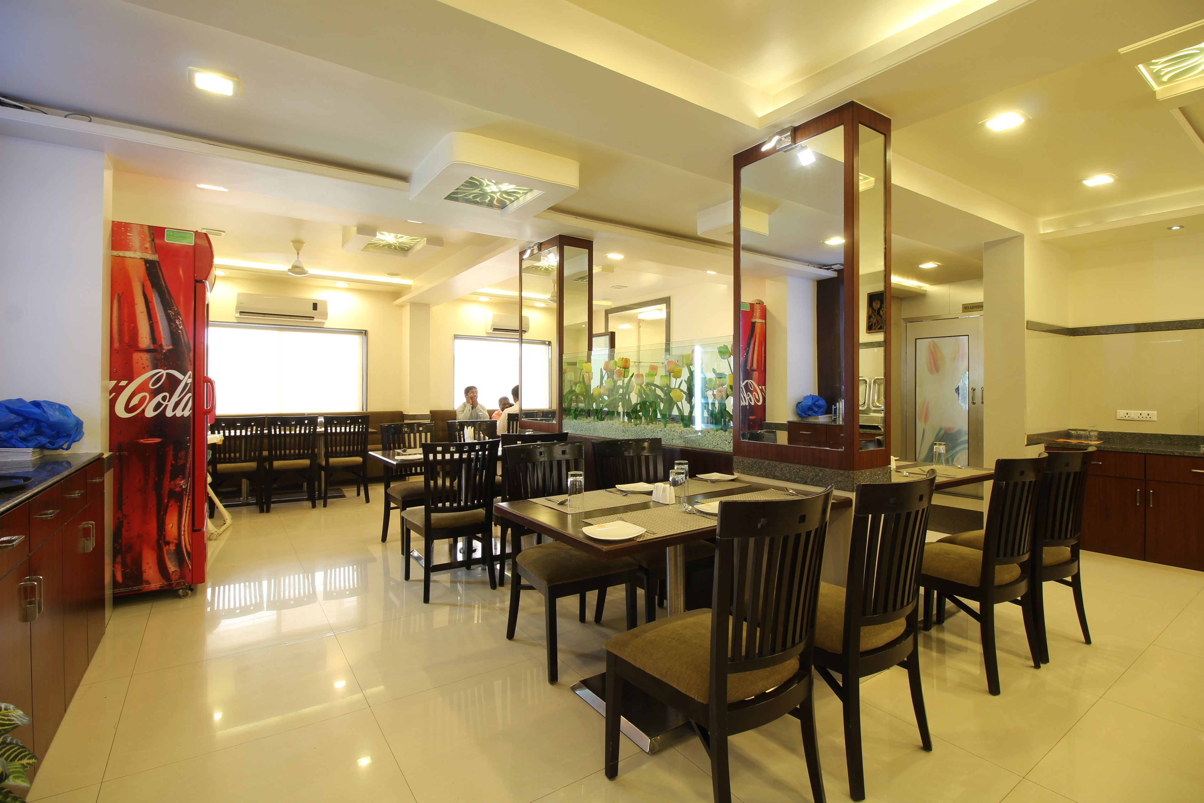 A dining area with tables and chairs, a Coca-Cola refrigerator, and a large mirror.