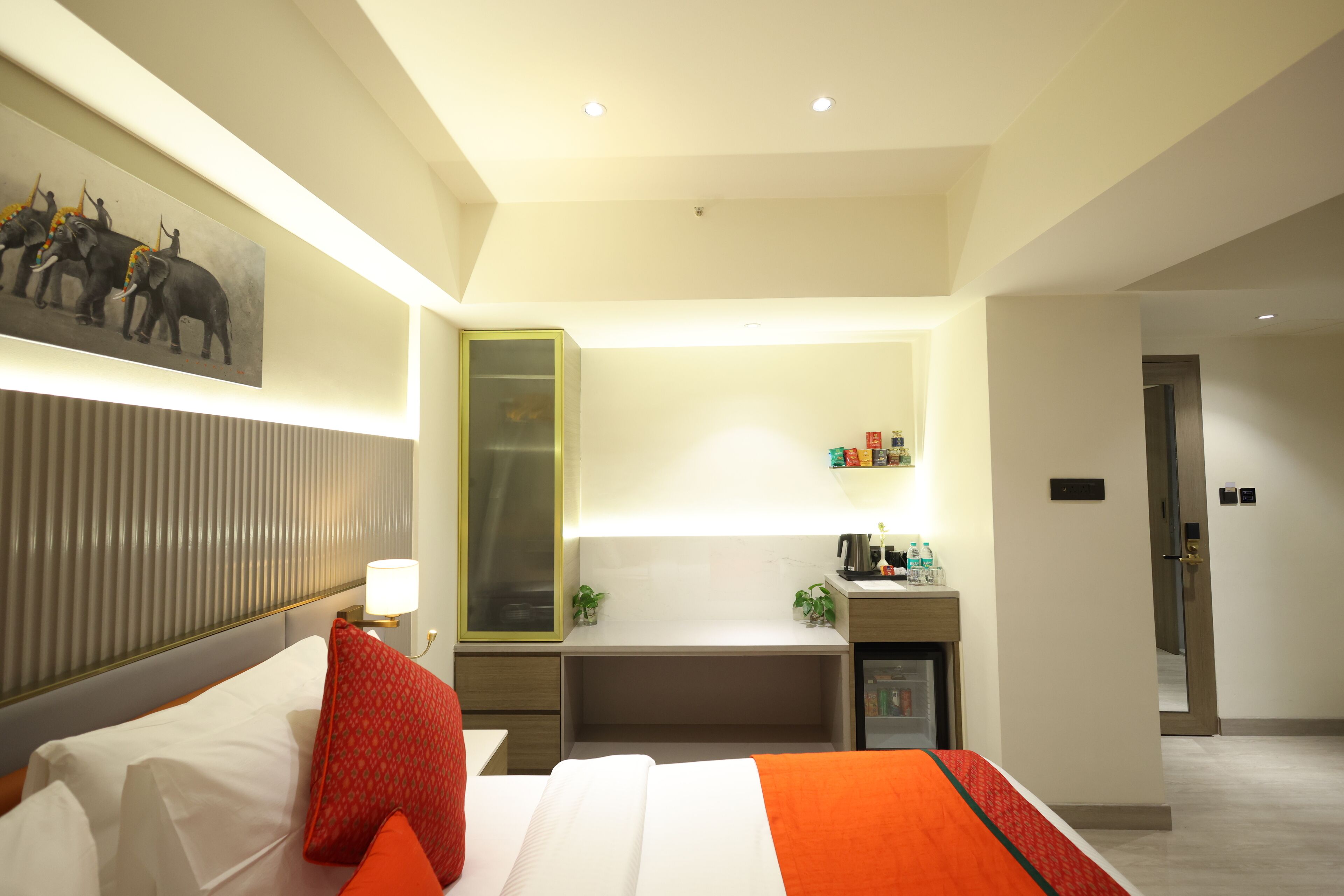 A hotel room with a bed, a desk, a minibar, and a wall-mounted TV.
