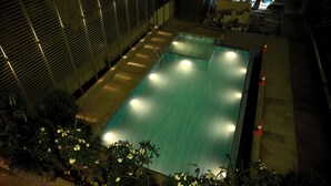 A swimming pool with a tiled deck, surrounded by plants and a metal fence. - Marigold- Newly Renovated Hotel (Rahata)