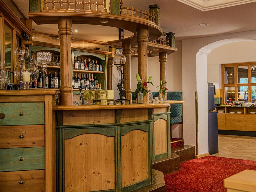 A bar area with wooden furniture, a red carpet, and a kitchen in the background.