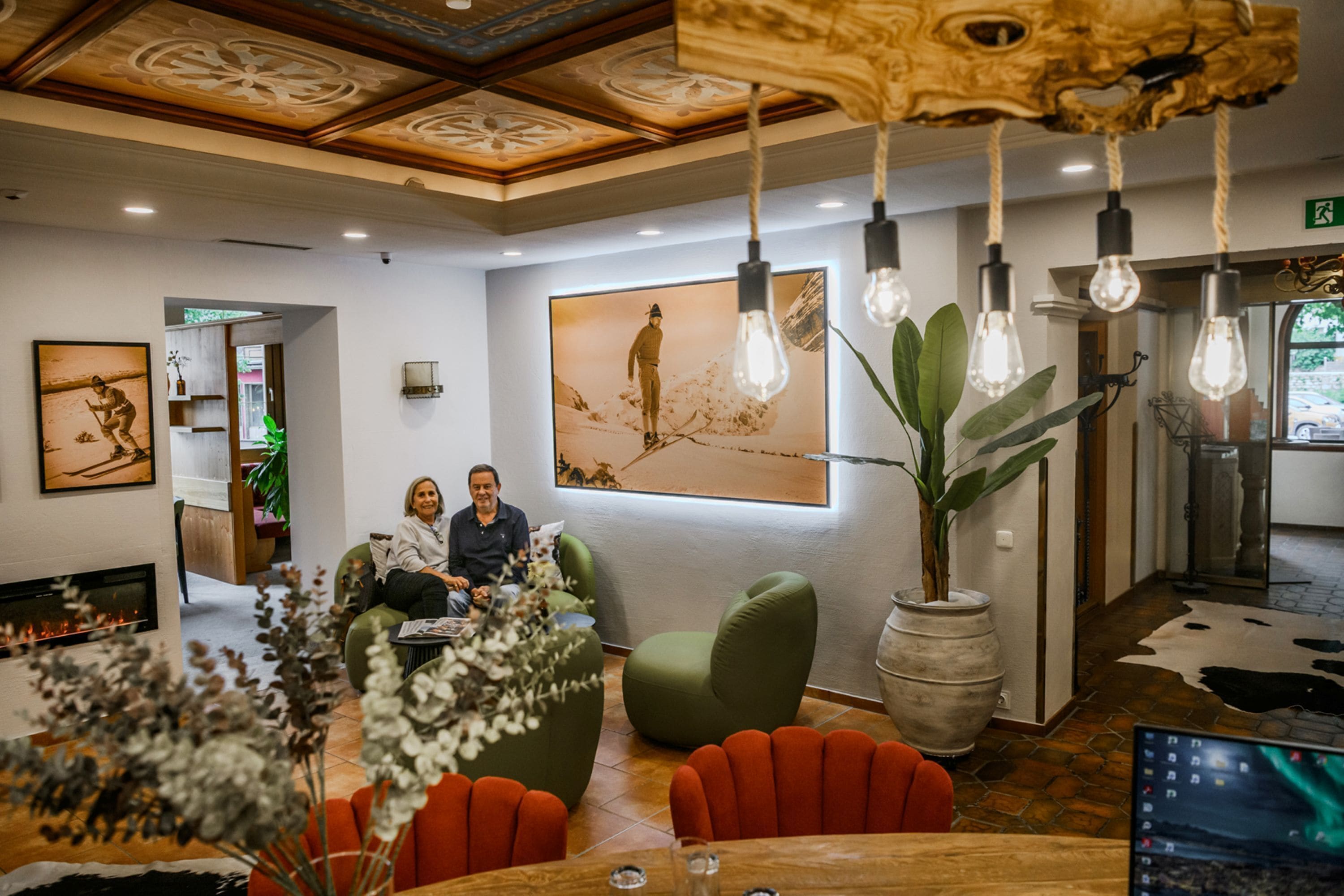 A modern interior with a fireplace, green and orange seating, a large plant, and a painting on the wall.