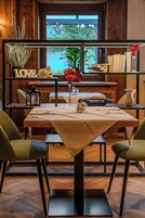 A dining area with a table set for two, a potted plant, a decorative glass, and a shelf with books and a 'LOVE' sign.