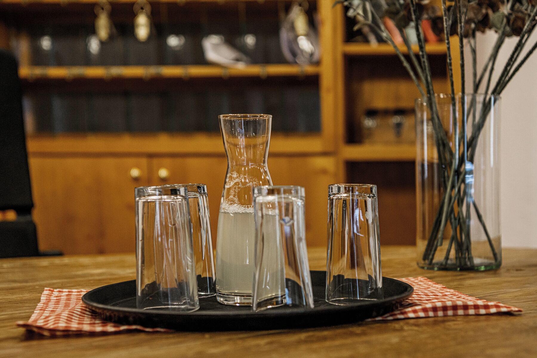 Una mesa con una jarrón, vasos, un mantel a cuadros y un fondo de madera.